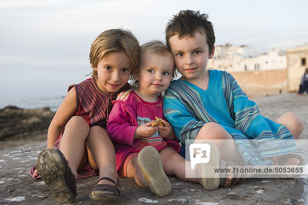 Junge Geschwister sitzen zusammen am felsigen Strand  Porträt