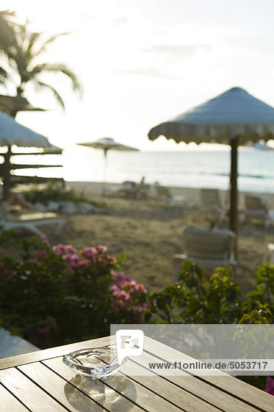 Aschenbecher am Tisch am Strand  Sonnenschirme und Liegestühle im Hintergrund