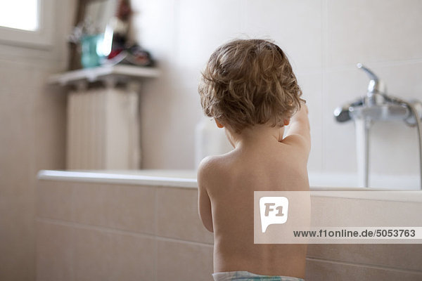 Toddler standing by bathtub playing  rear view