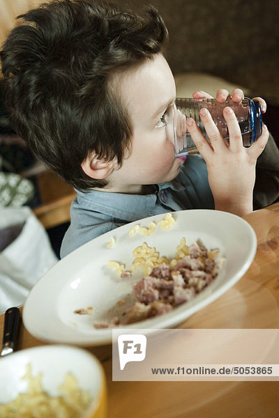 Kleiner Junge am Tisch  trinkt ein Glas Wasser.