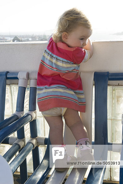 Kleinkind auf Stuhl stehend  Blick über Balkongeländer  Rückansicht