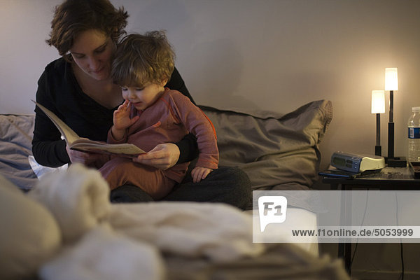 Mother holding toddler son on lap  reading bedtime story in bed