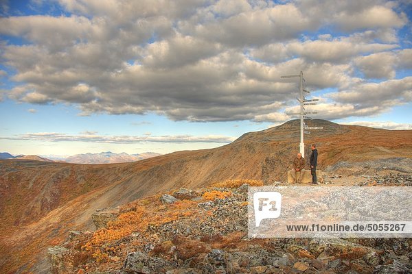 Two people  father and son standing at the signpost on top of Keno hill  Yukon. The Werneke mountains are oin the distance.