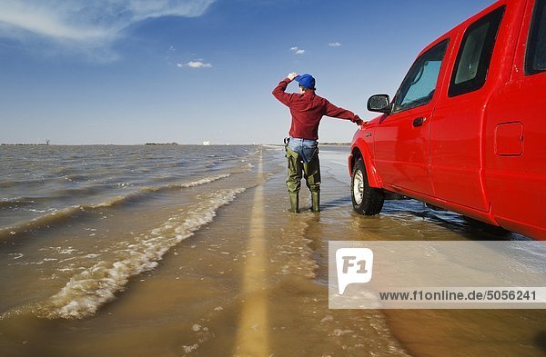 a man wearing waders looks out over huge amounts of farmland in the Red River Valley flooded by water from the Red River  Highway 75 near Morris  Manitoba  Canada