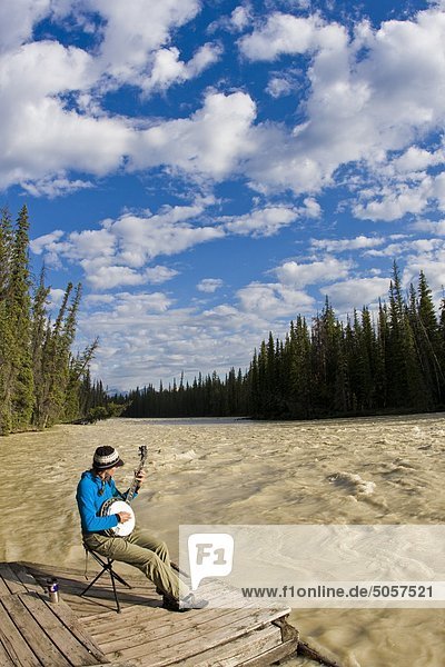 Female kayaker takes a break from paddling to play her banjo along the Athabasca River  Jasper National Park  Alberta  Canada