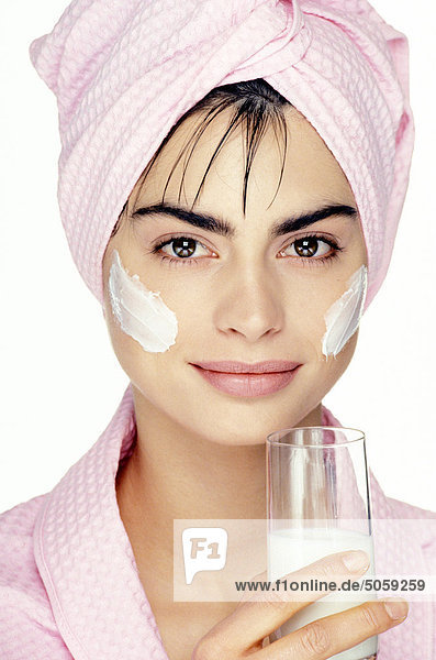 Junge Frau mit Creme auf ihrem Gesicht ein Glas Milch in der hand