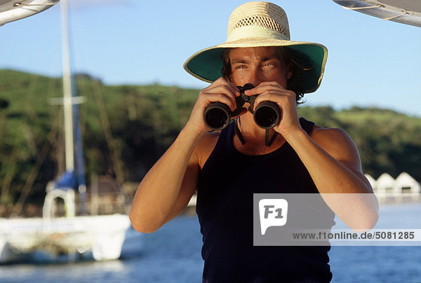 Australien  Queensland  Whitsunday Islands  Mann mit einem Fernglas auf einem Boot an Lindeman Insel