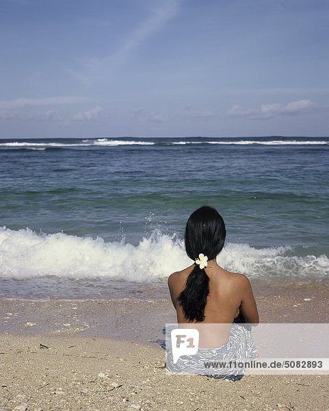 Frau sitzt am Strand  Rückansicht