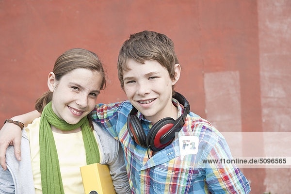 Lächelnder Junge mit Kopfhörer und Mädchen mit Mappe umarmen sich