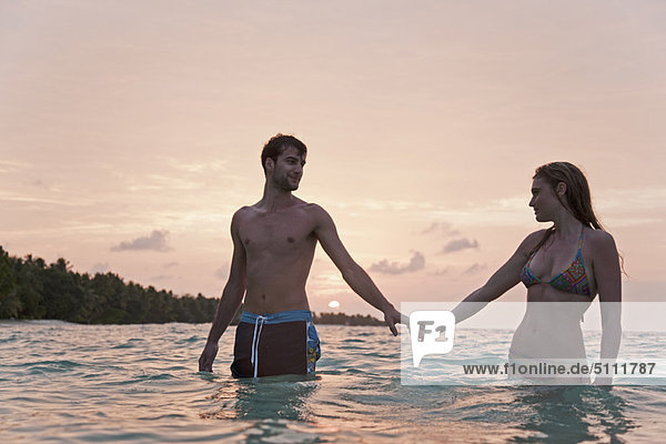 Couple holding hands in water at beach