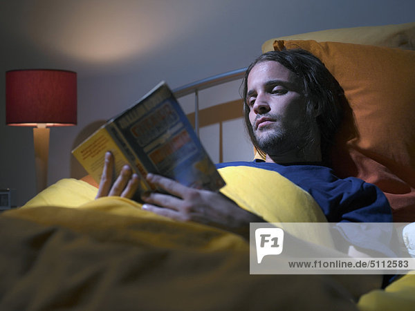 Mann liest ein Buch im Bett
