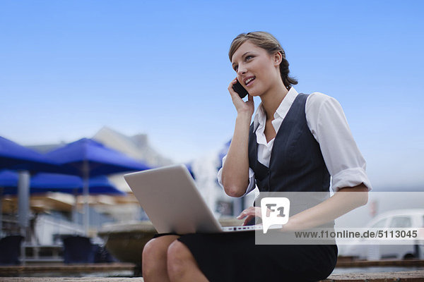 Businesswoman with laptop on cell phone