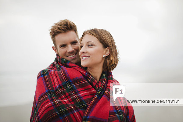 Couple wrapped in blanket on beach