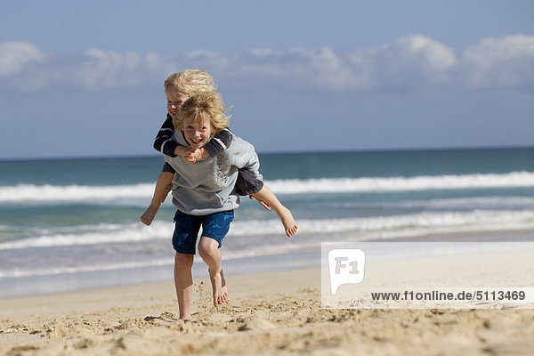 Boy carrying brother piggyback on beach