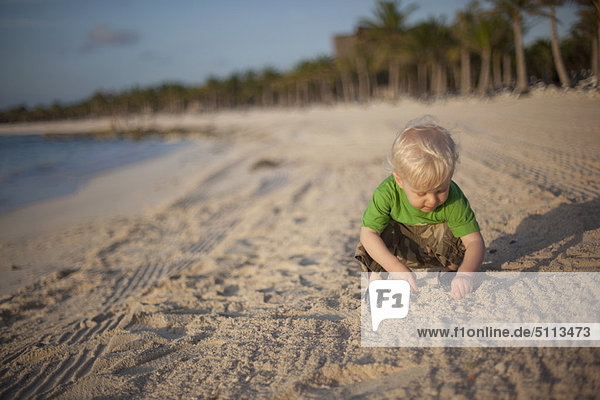 Toddler boy playing with sand on beach