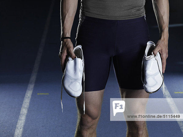 Man carrying running shoes on track