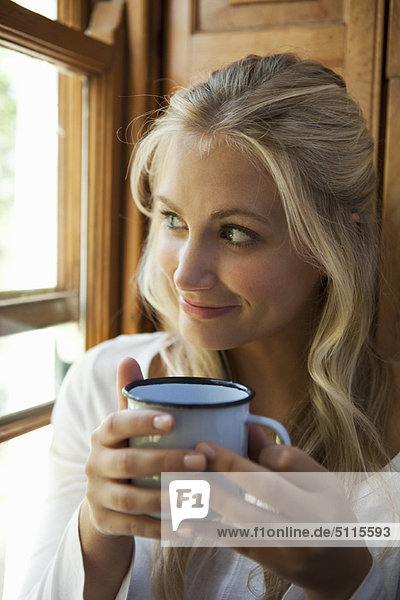 Woman having cup of coffee by window