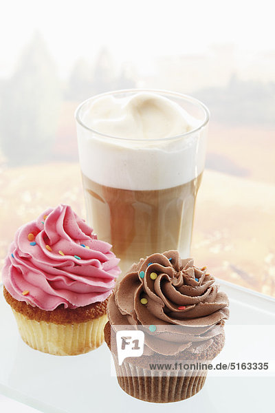 Close up of buttercream cupcakes with glass of latte macchiato