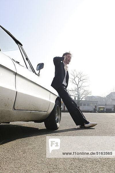 Mittlerer Erwachsener Mann  der sich auf ein Oldtimer-Auto stützt und ein Handy benutzt.