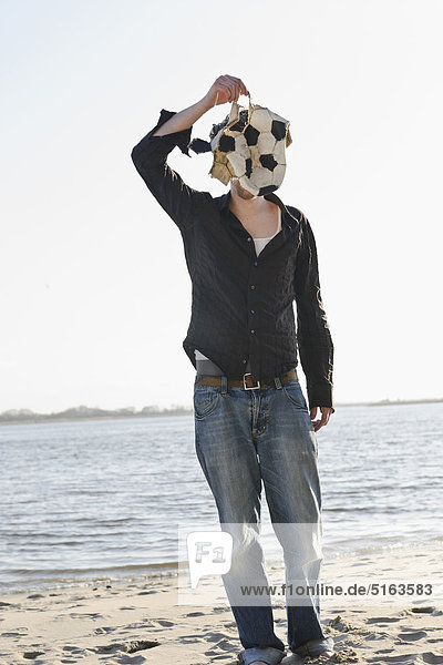 Ein erwachsener Mann bedeckt sein Gesicht mit zerrissenem Fußball an der Elbe.