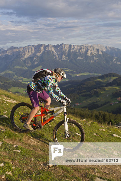 Österreich  Tirol  Spitzstein  Junge Frau Mountainbiken am Hang mit Kaisergebirge im Hintergrund