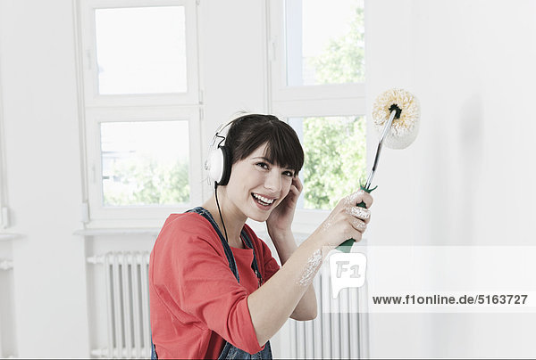 Young woman listening music and painting with roll brush
