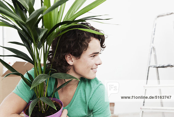 Junger Mann mit Topfpflanze bei der Renovierung der Wohnung