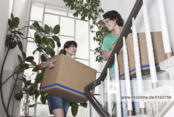 Deutschland  Köln  Junges Paar mit Karton auf der Treppe in renovierter Wohnung