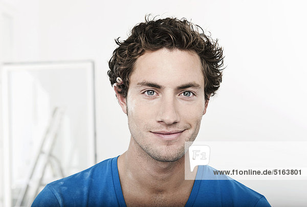 Nahaufnahme eines jungen Mannes mit Bleistift hinter dem Ohr in der renovierenden Wohnung  Portrait  lächelnd