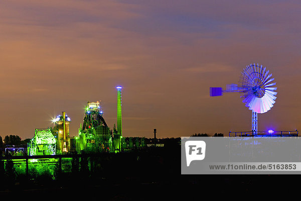 Germany Nordrhein-Westfalen Duisburg Duisburg-Nord Landscape Park View of illuminated blast furnace and wind mill of industrial plant at night