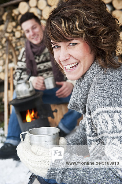 Österreich  Salzburger Land  Flachau  Junger Mann und Frau machen Tee und sitzen im Winter neben dem Herd.