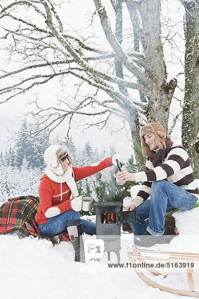 Österreich  Salzburger Land  Flachau  Junger Mann und Frau machen Tee und sitzen im Winter neben dem Herd.