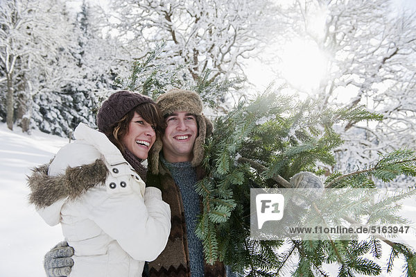 Österreich  Salzburger Land  Flachau  Junger Mann und Frau mit Weihnachtsbaum im Schnee