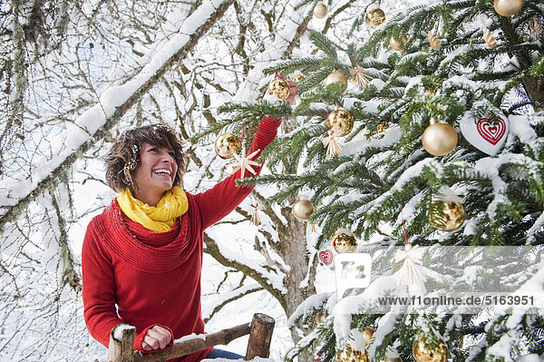 Österreich  Salzburger Land  Flachau  Junge Frau schmückt Weihnachtsbaum im Winter