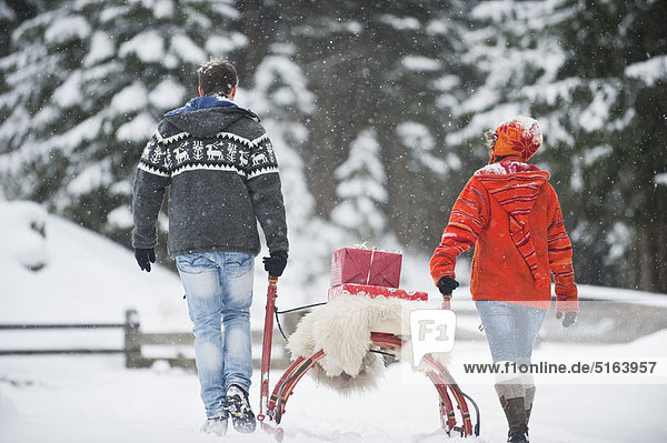 Österreich  Salzburger Land  Flachau  Junger Mann und Frau mit Weihnachtspäckchen auf Schlitten im Schnee