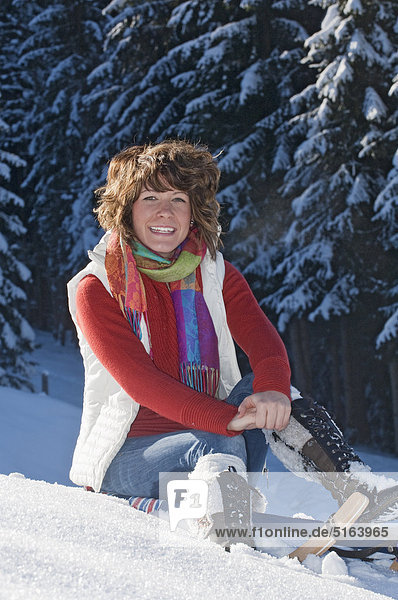 Austria  Salzburg Country  Flachau  Young woman sitting on sledge in snow