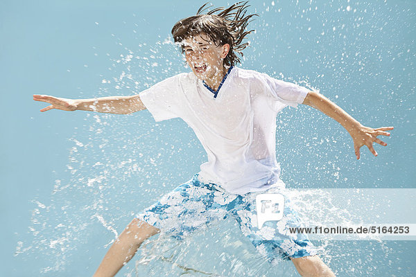 Germany  Boy jumping in splash of water against blue background
