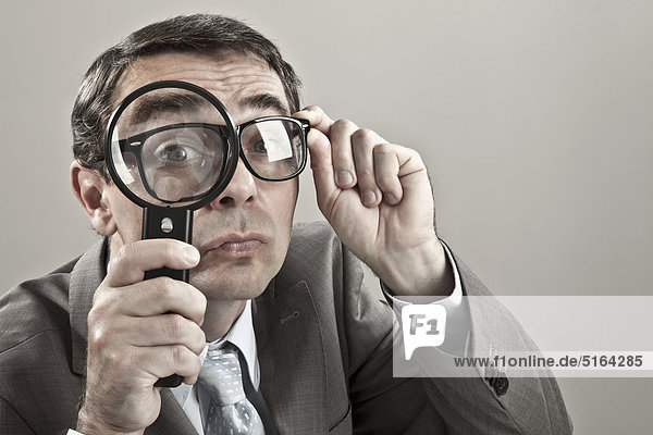 Close up of mature businessman looking through magnifying glass against grey background