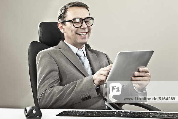 Businessman holding ipad and smiling against grey background