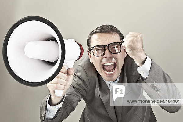Close up of businessman screaming through megaphone against grey background