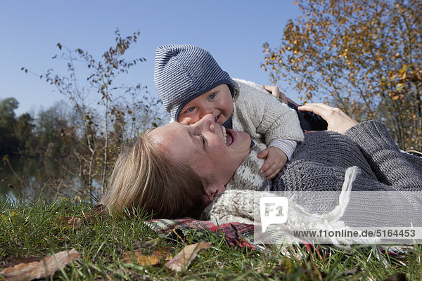 Deutschland  Bayern  München  Mutter mit Kind auf Gras liegend  lachend