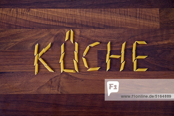 Nahaufnahme des Wortes Küche geschrieben mit Penne auf Holzuntergrund