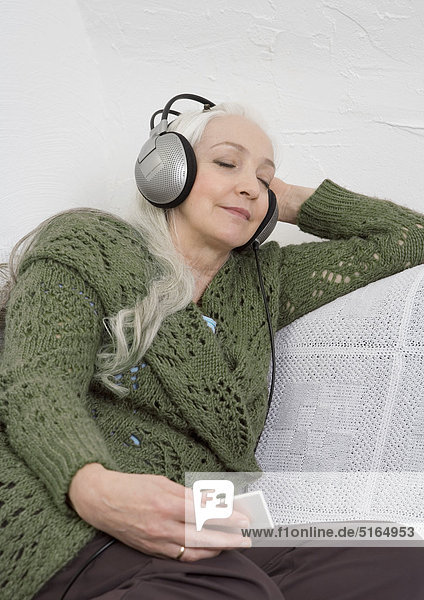 Frau hört MP3-Player auf dem Sofa,  lächelnd