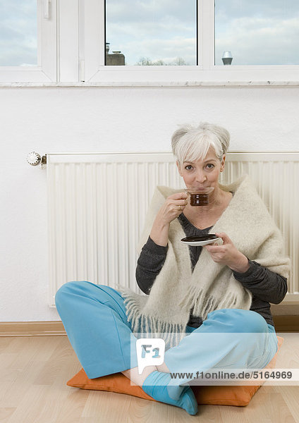 Frau trinkt Tee in der Nähe der Heizung zu Hause  lächelnd  Porträt