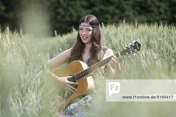 Young woman with guitar in corn field