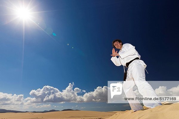 Black belt martial artist training on desert dunes