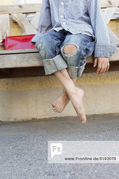 Close up of boy’s bare feet on bench
