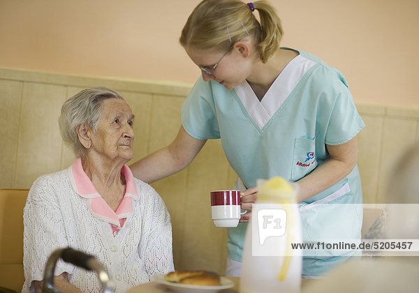 Altenheim  Pflegerin bringt Seniorin eine Tasse