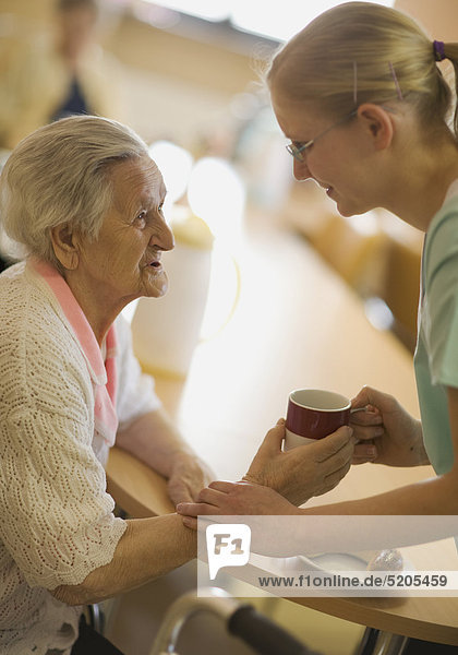 Altenheim  Pflegerin gibt Seniorin eine Tasse