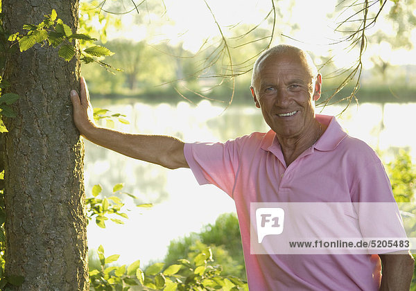 Senior steht an See neben einem Baum